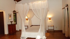A bedroom with a four-poster bed, two bedside lamps, and a wooden floor. - Ging Oya Lodge (Wennappuwa)