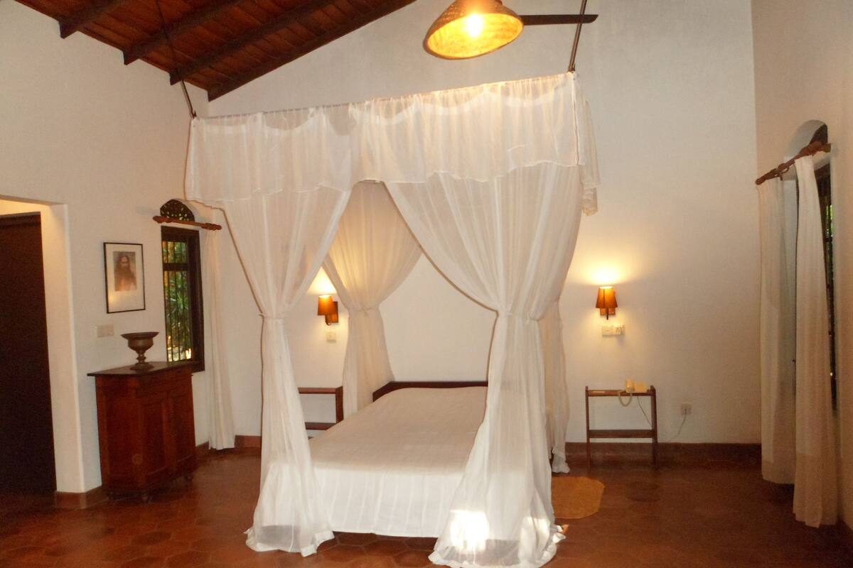A bedroom with a four-poster bed, two bedside lamps, and a wooden floor.