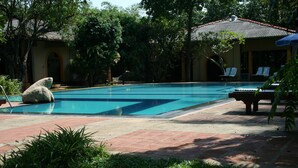 A swimming pool with a stone sculpture, surrounded by greenery and a building with a tiled roof. - Ging Oya Lodge (Wennappuwa)