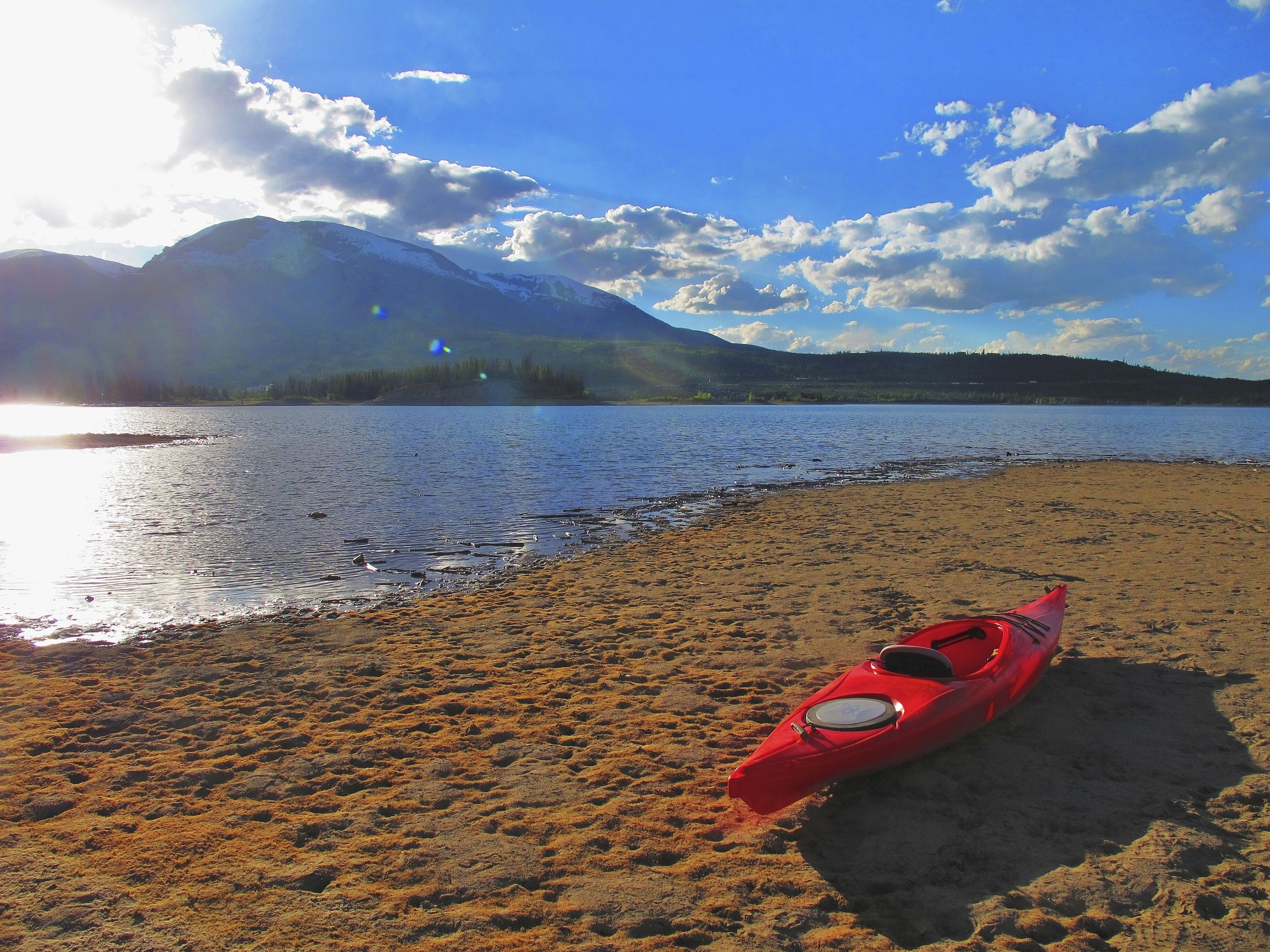 Un kayak sur une plage de sable, avec un lac et des montagnes en arrière-plan.