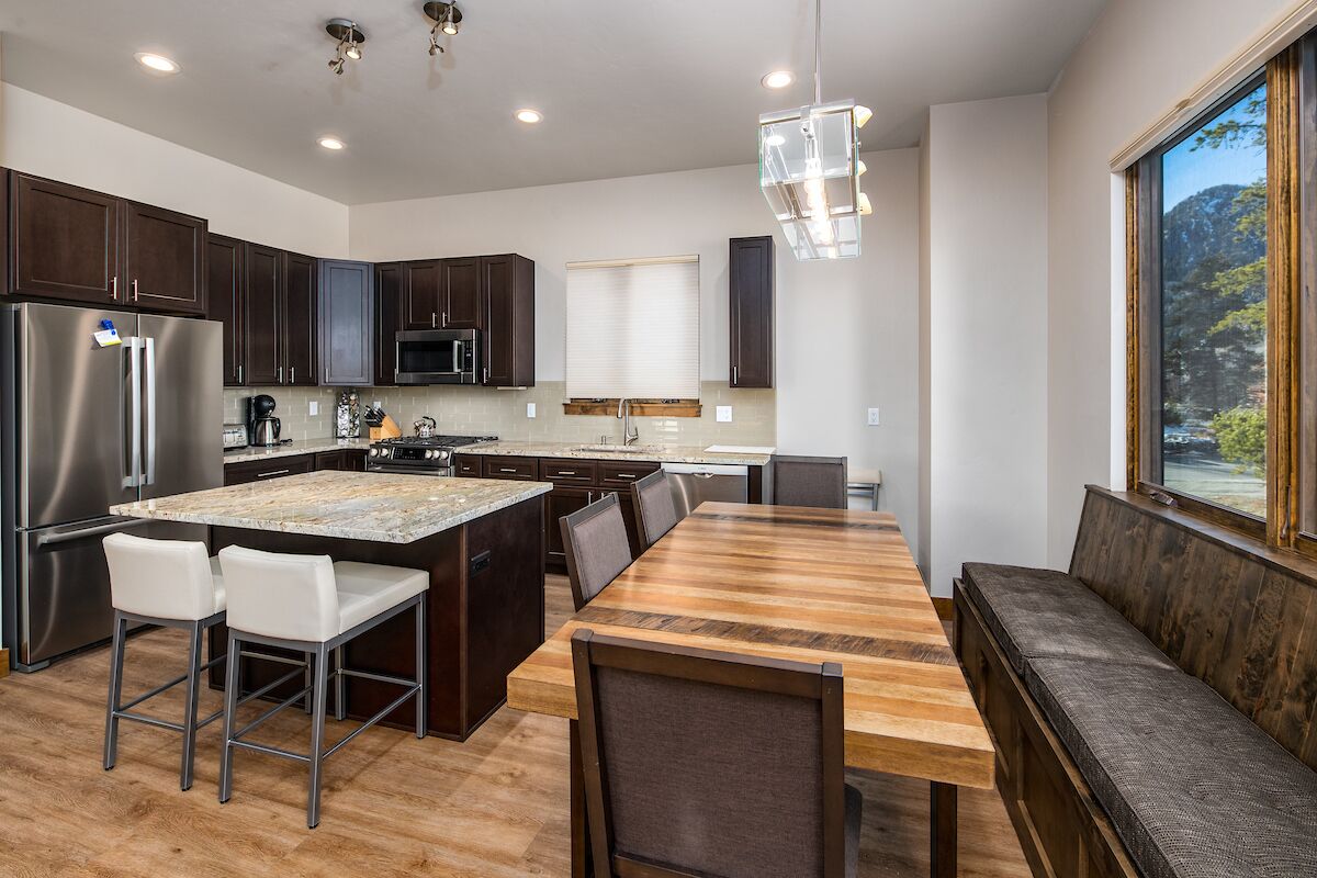Una cocina moderna con armarios de madera oscura, un refrigerador de acero inoxidable, una mesa de comedor de madera y una isla integrada con taburetes de bar.