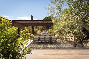 Um pátio externo com deck de madeira, pérgola e área de refeições com cadeiras e mesa.