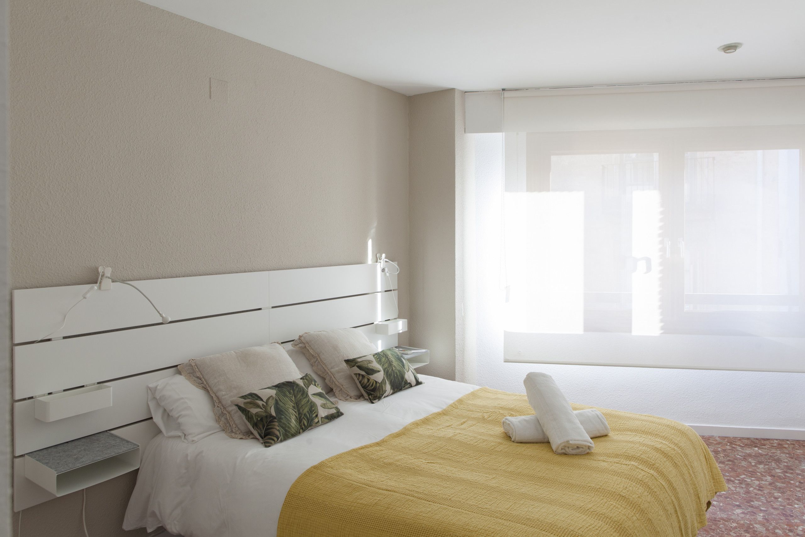 Een hotelkamer met een bed, nachtkastje en een raam met gordijnen.