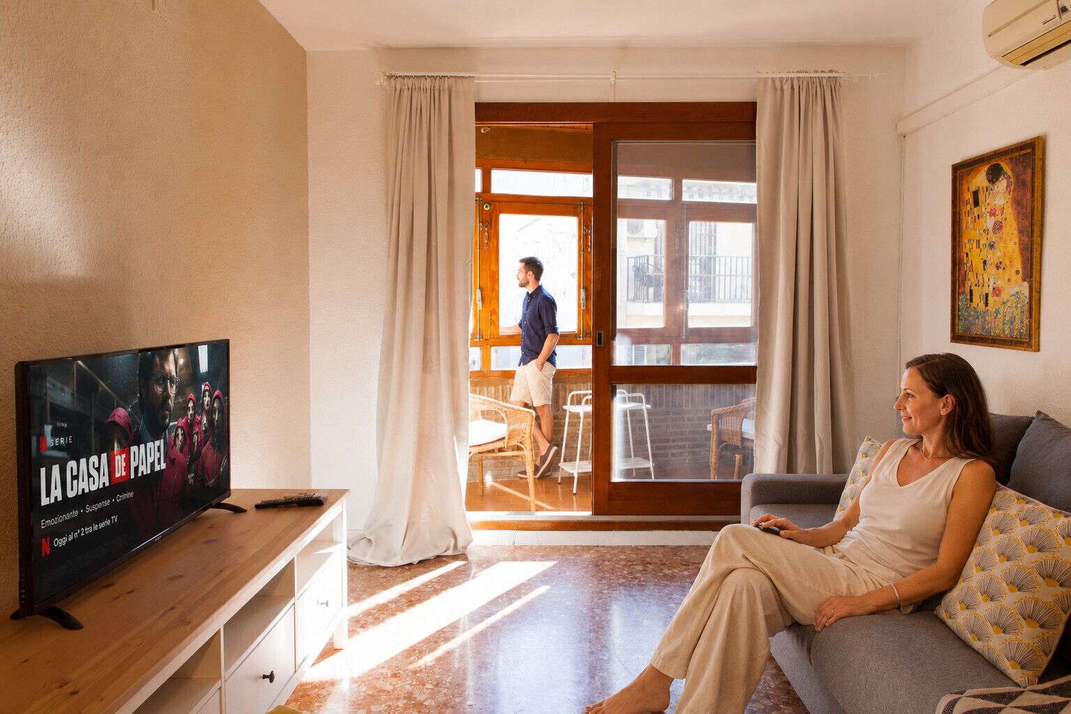 Un soggiorno con televisore, un divano e una persona seduta.