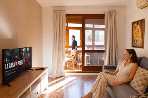 A living room with a television, a sofa, and a person sitting on the sofa.