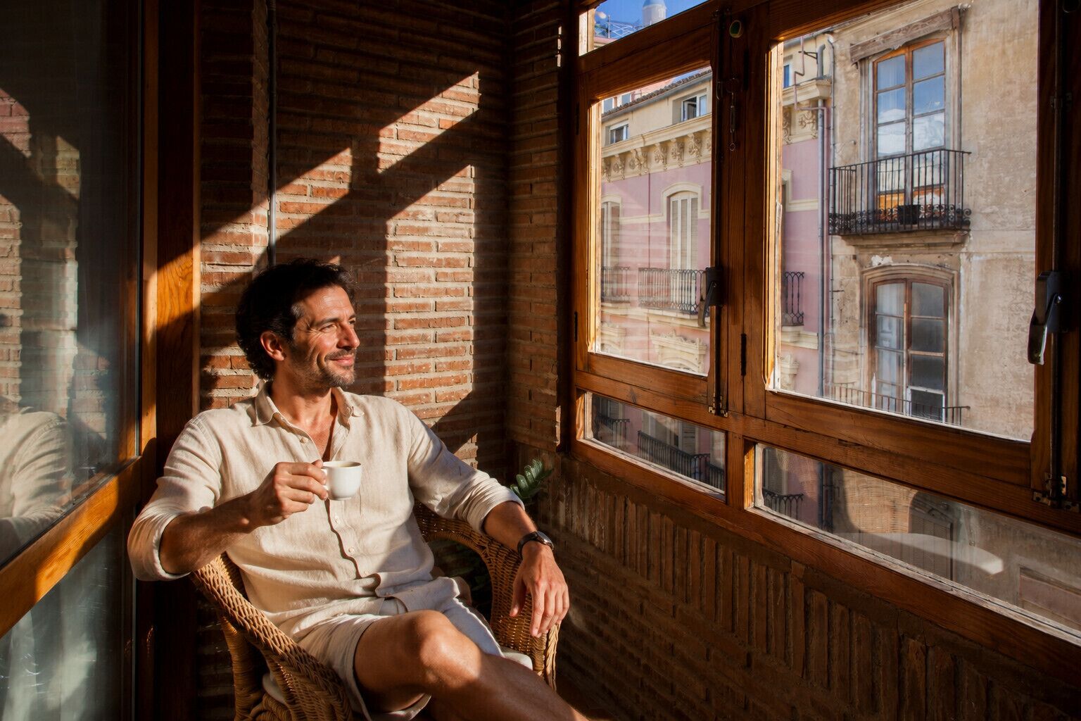Una persona seduta vicino a una finestra con vista su un edificio, pareti di legno e una struttura in mattoni all'esterno.
