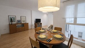 Een eetgedeelte met een ronde tafel gedekt voor vier personen, een televisie op een standaard en kunst aan de muur.