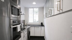 Een moderne keuken met roestvrijstalen apparatuur, een ingebouwde oven, een wasmachine en een raam voor natuurlijk licht.