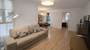 Een moderne woonkamer met een bank, een eethoek en een keuken op de achtergrond.