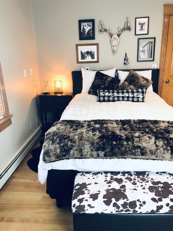 Quarto com cama, mesa de cabeceira, abajur e decorações nas paredes, incluindo quadros e um crânio de animal montado.
