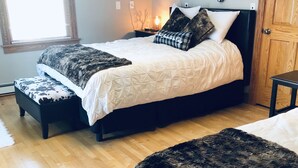A bedroom with two beds, a wooden floor, a window with blinds, and wall-mounted artwork. - Large home walking distance to town and trails. 10 minutes to ski resorts. (Ironwood)