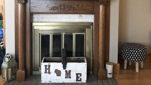 A fireplace with a ship model, a wooden chest labeled "HOME", and a patterned ottoman. - Large home walking distance to town and trails. 10 minutes to ski resorts. (Ironwood)