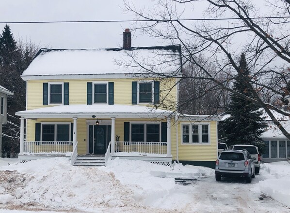 Une maison jaune à deux étages, avec un porche blanc et une cheminée.