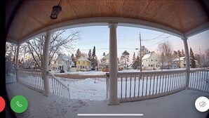 A covered porch with a view of a snow-covered street and houses. - Large home walking distance to town and trails. 10 minutes to ski resorts. (Ironwood)