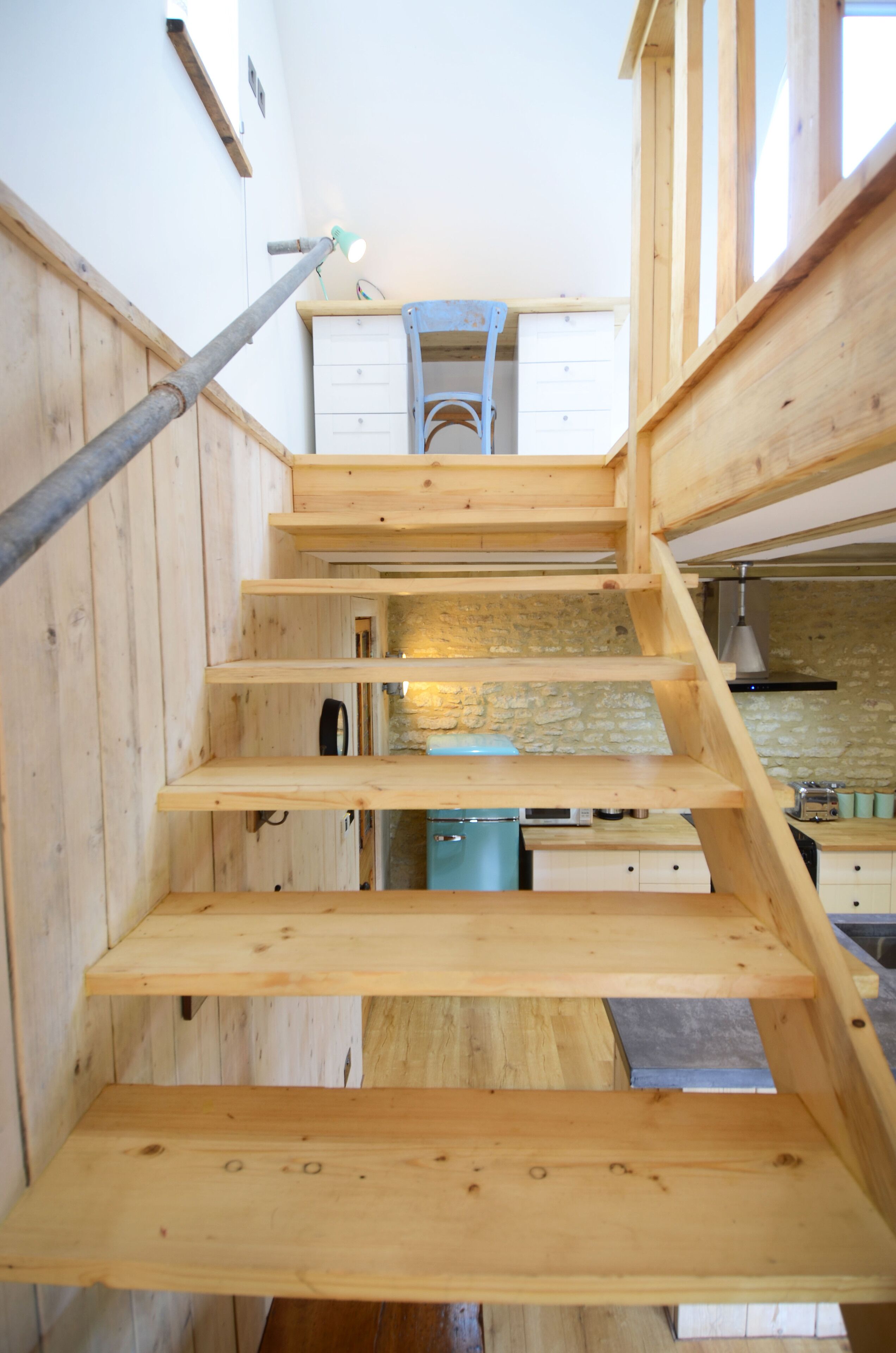 A wooden staircase leading to a kitchen area with a stone wall and a blue appliance.