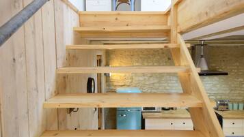 A wooden staircase leading to a kitchen area with a stone wall and a blue appliance.