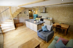 Une cuisine chaleureuse avec un plancher en bois, un coin repas avec une table et des chaises, un canapé gris et un escalier menant à un niveau supérieur.