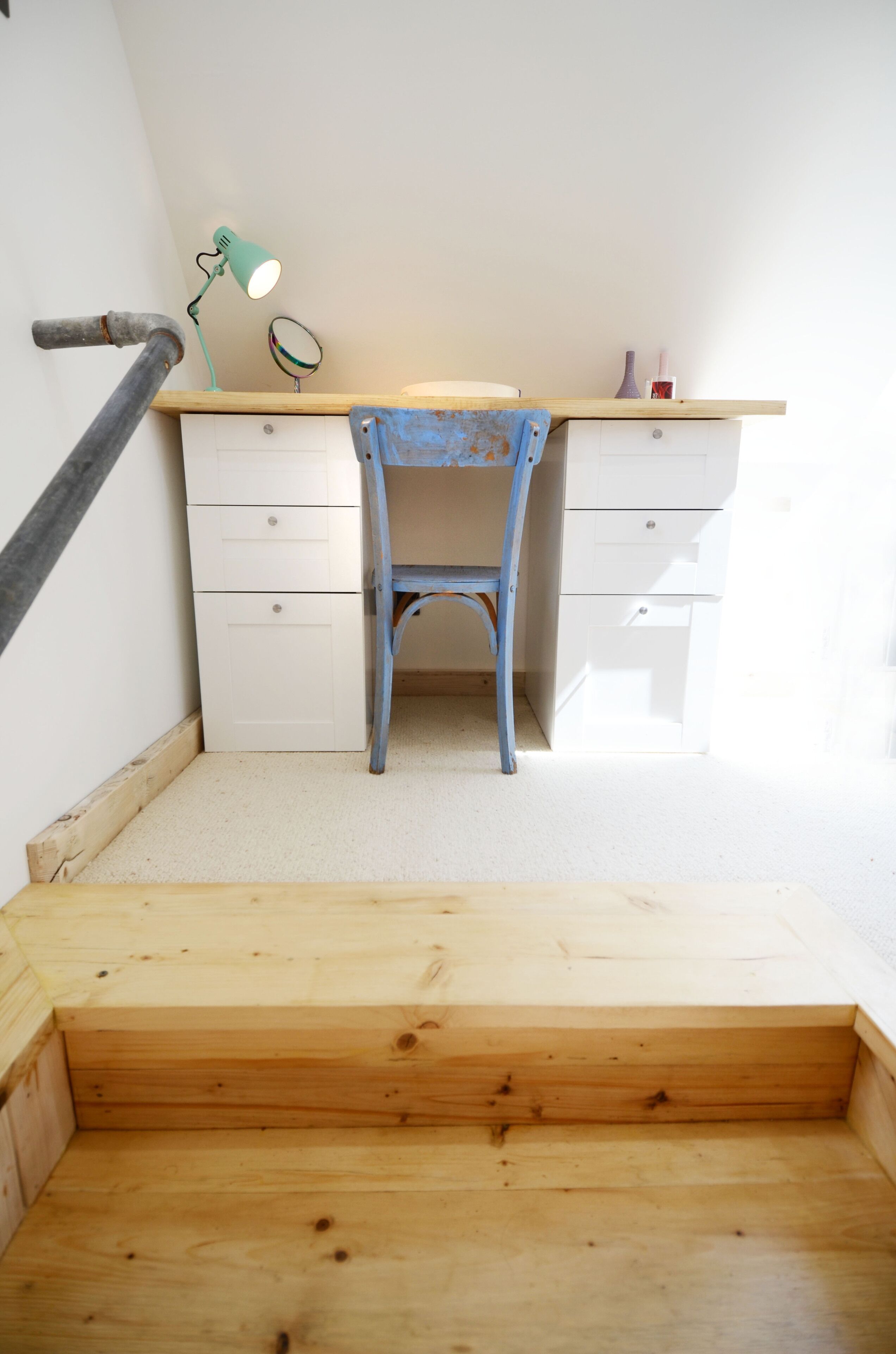 Ein Eckzimmer mit einem Holztisch, einem Stuhl, einem kleinen Spiegel und einer Lampe.