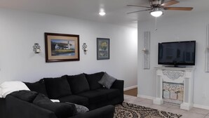 Ein Wohnzimmer mit einer schwarzen Couch, einem Kamin, einem Fernseher und zwei gerahmten Bildern an der Wand.