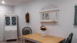 Ein Essbereich mit einem Holztisch, Stühlen, einem weißen Schrank mit Glastüren, einem Wandspiegel und einer Vase mit Blumen.