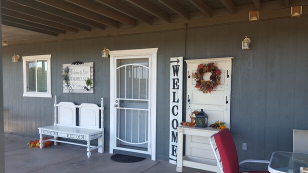 Eine überdachte Veranda mit einer weißen Bank, einem roten Sessel, einem weißen Tisch und einem Schild mit der Aufschrift 'WELCOME'.