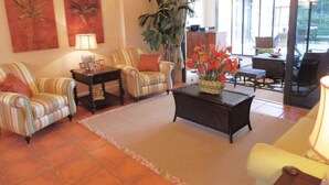 A living room with striped armchairs, a coffee table with a vase of flowers, and a large plant. - Privacy in Paradise, full refund*, heated pool, sleeps 6 (Rotonda West)