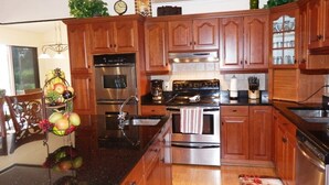 A kitchen with wooden cabinets, stainless steel appliances, and a fruit basket on the counter. - Privacy in Paradise, full refund*, heated pool, sleeps 6 (Rotonda West)