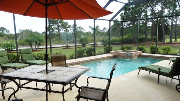 A covered outdoor area with a pool, green chairs, and a table. - Privacy in Paradise, full refund*, heated pool, sleeps 6 (Rotonda West)