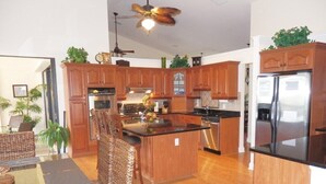 A modern kitchen with wooden cabinets, a central island, stainless steel appliances, and a ceiling fan. - Privacy in Paradise, full refund*, heated pool, sleeps 6 (Rotonda West)
