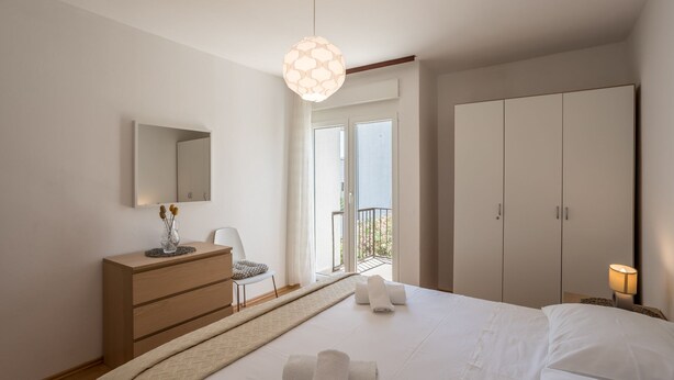 Una camera da letto con un letto, una cassettiera, una sedia, un armadio e un balcone con vista.