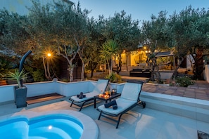 Un área junto a la piscina con sillones reclinables, un jacuzzi y una terraza con iluminación ambiental.