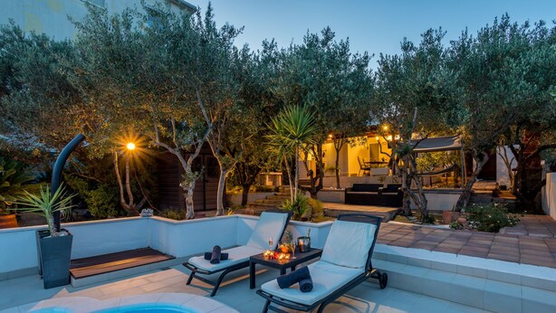 Un área junto a la piscina con sillones reclinables, un jacuzzi y una terraza con iluminación ambiental.