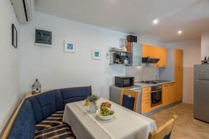 A compact kitchen with modern appliances, a dining area with a blue sofa, and a small table set with a bowl of fruit. - Detached House on a plot of 500m2 with private pool and a walled Oliva garden (Stari Grad)