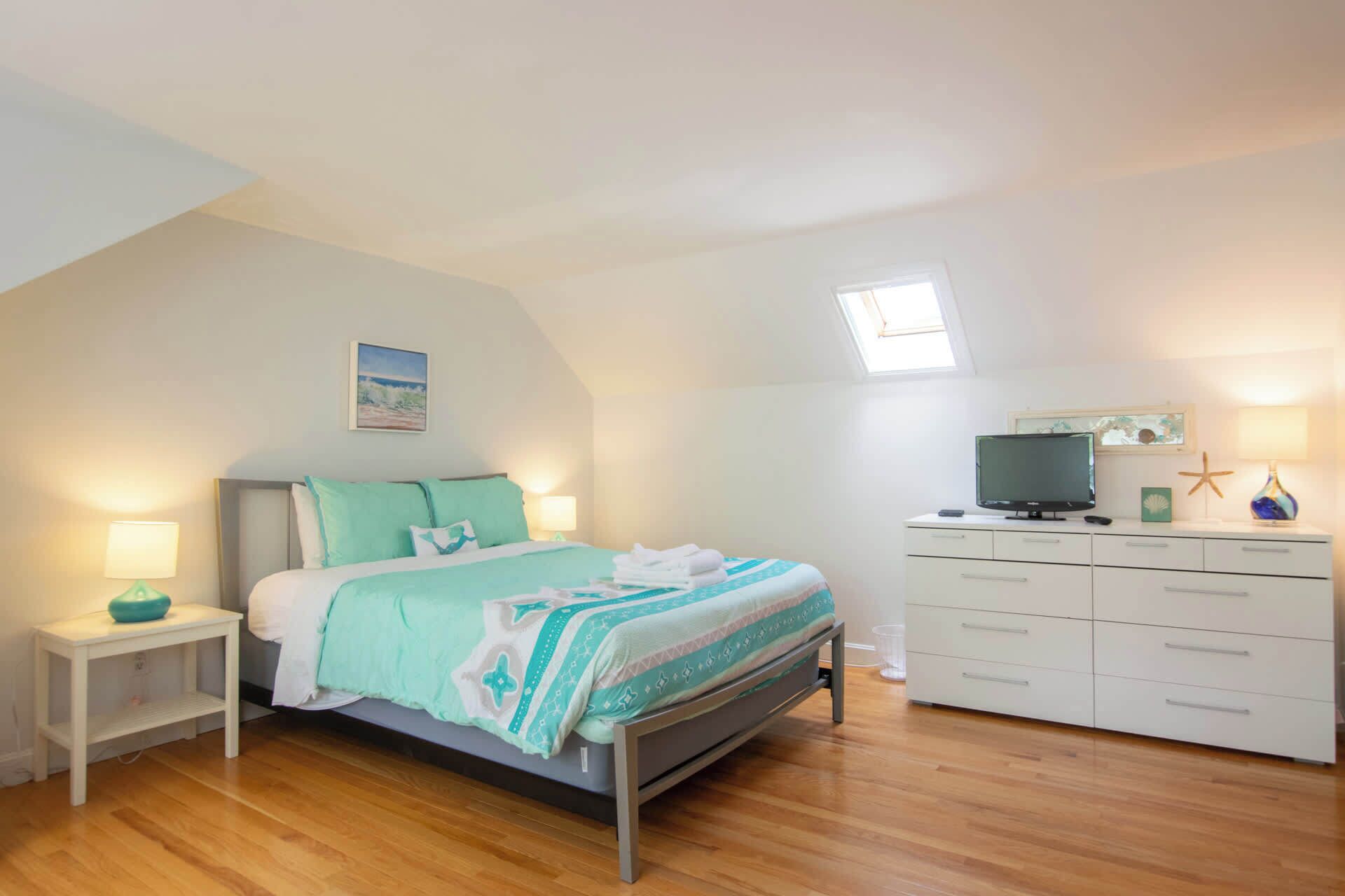 A bedroom with a bed, bedside tables, a dresser, a TV, and a starfish decoration.