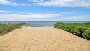Une plage de sable fin offrant une vue dégagée sur l’océan et un ciel bleu parsemé de nuages.