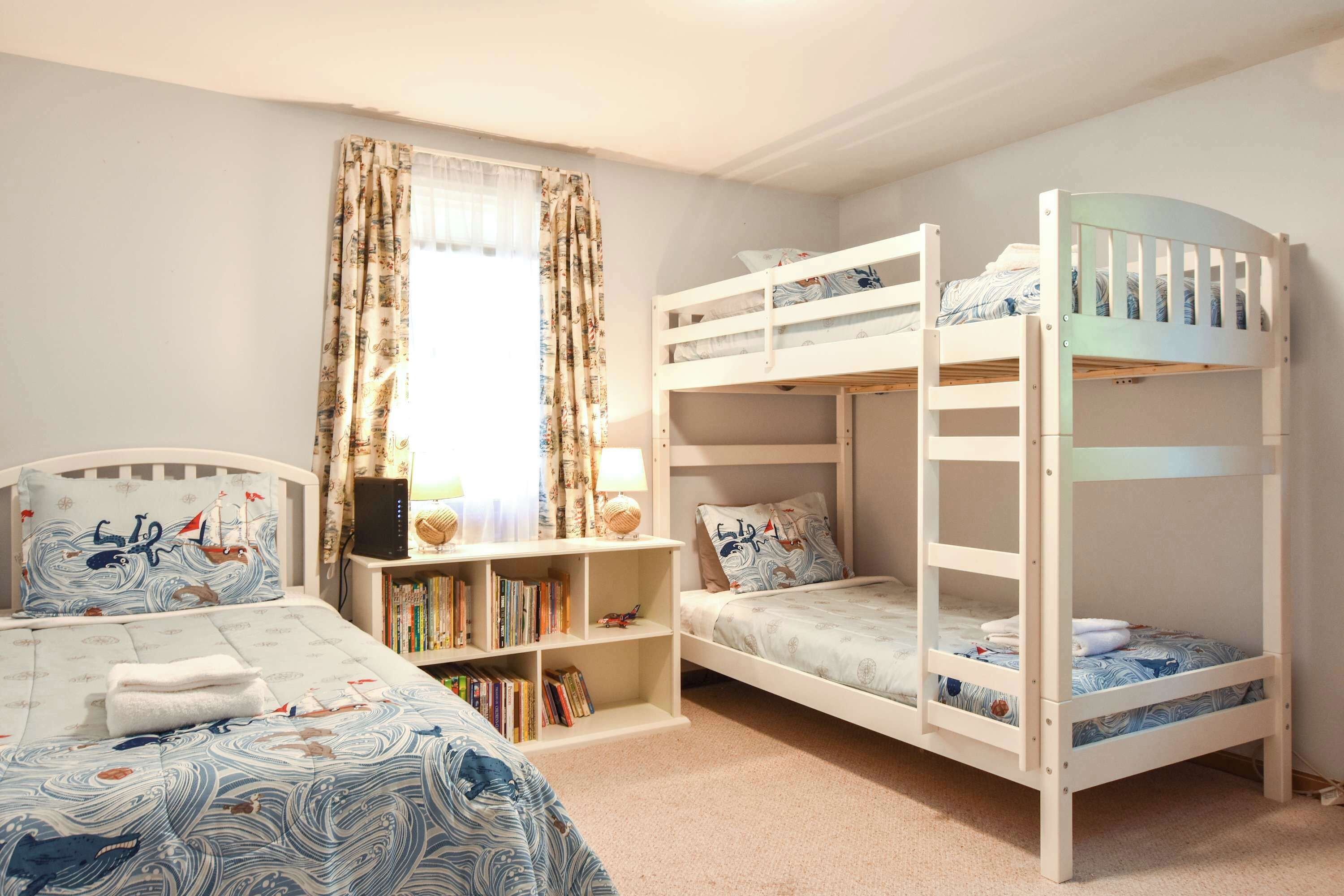 Une chambre d’enfant avec des lits superposés, une bibliothèque et un lit recouvert d’une couvre-lit sur le thème de la marine.