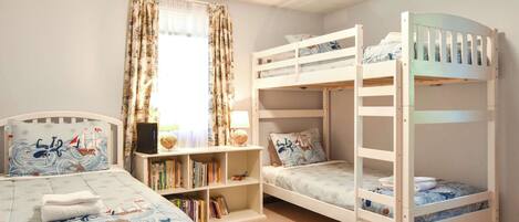 Une chambre d’enfant avec des lits superposés, une bibliothèque et un lit recouvert d’une couvre-lit sur le thème de la marine.