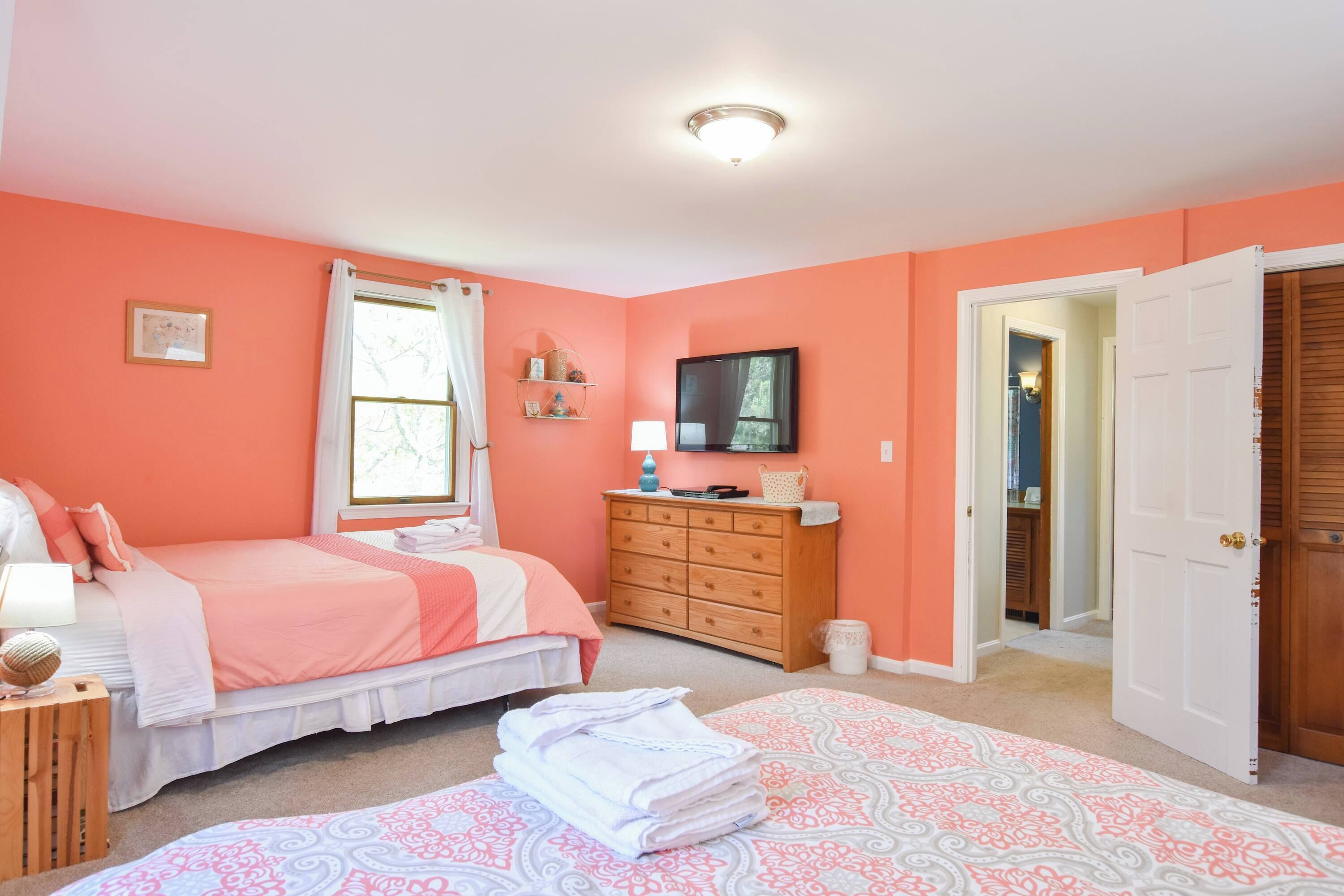 A bedroom with two beds, a dresser, a television, and a door leading to another room.