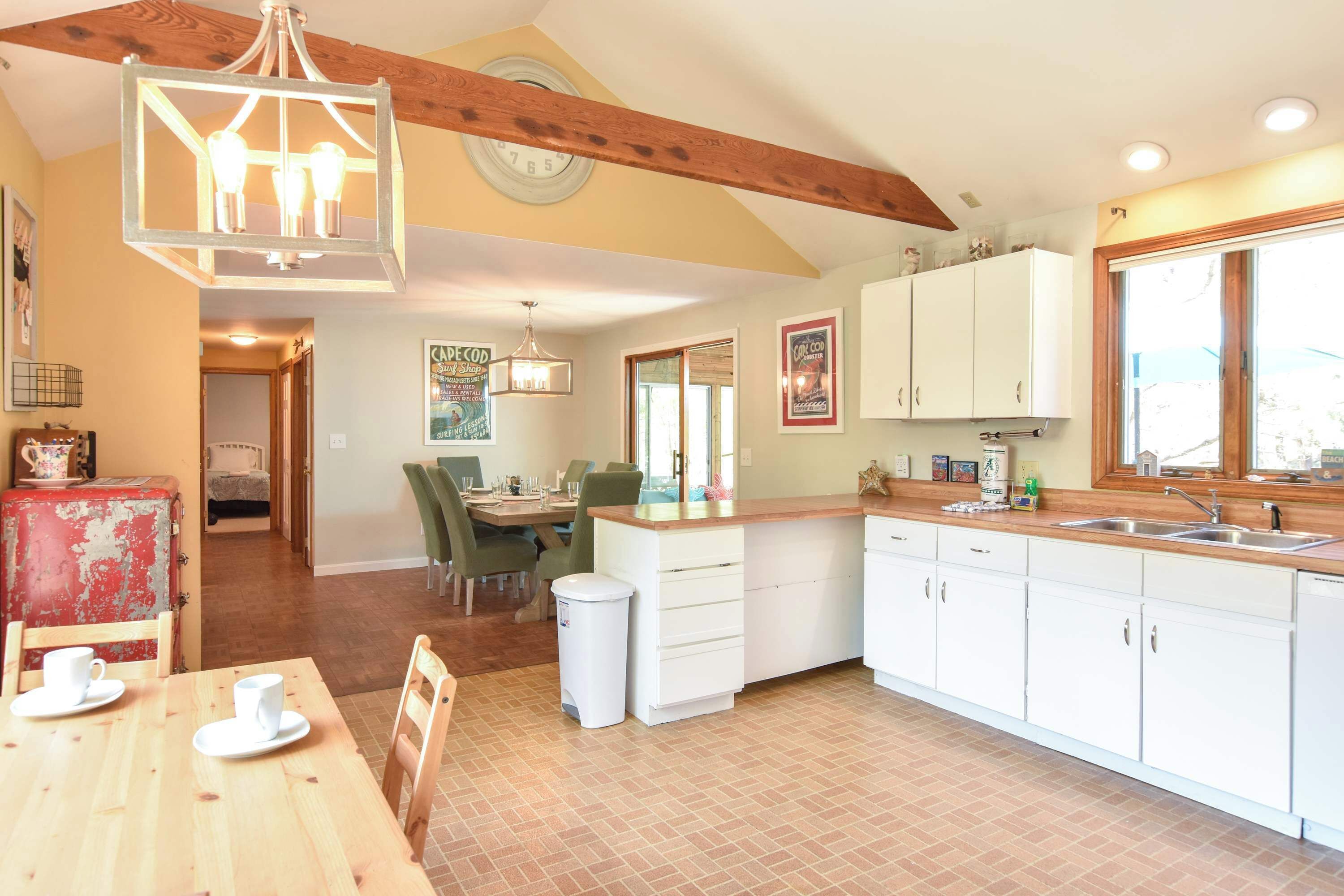 A spacious kitchen with white cabinets, a wooden dining table, and a hanging light fixture.