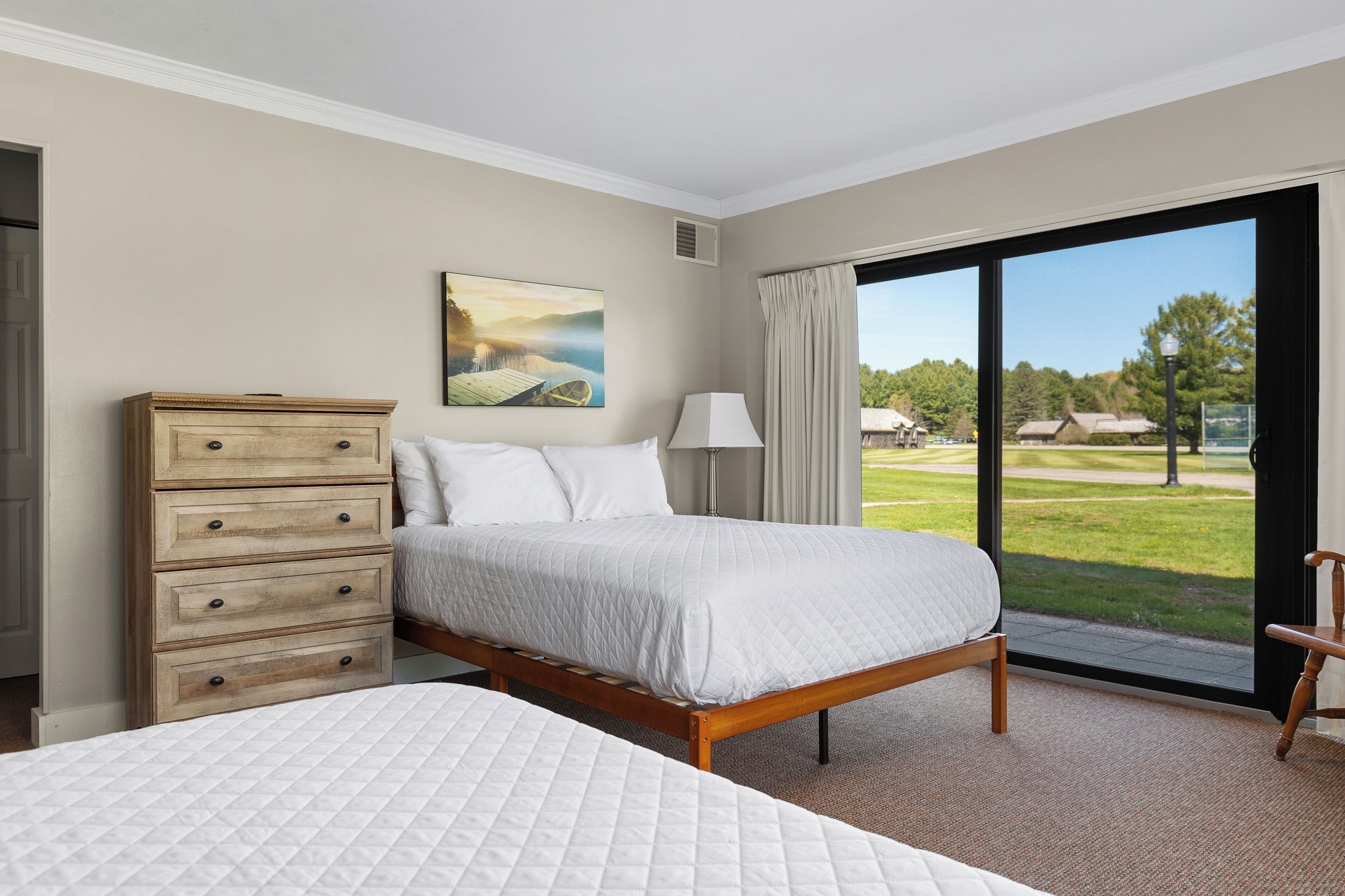 A hotel room with a large bed, a wooden dresser, a painting, and a view of a golf course through the window.