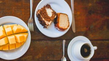 A table with a plate of mango slices, a slice of cake, a cup of coffee, and cutlery.