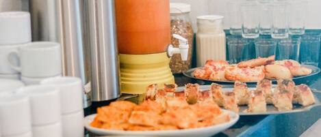 A buffet table with various food items, including pizza and bread, and beverage dispensers.