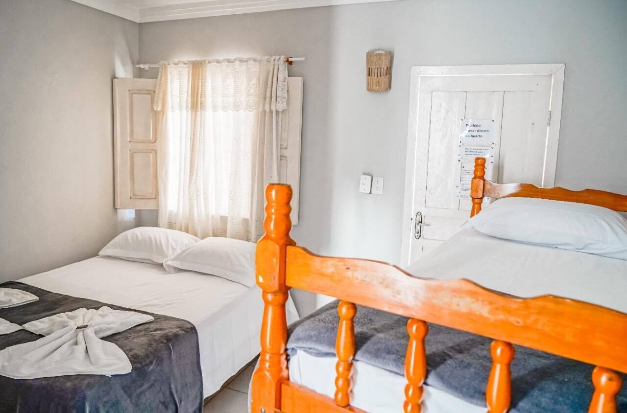 A bedroom with two beds, one with an orange headboard, and a window with curtains.