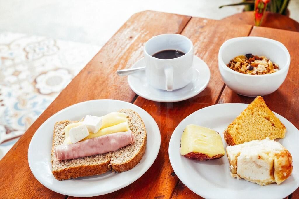 Une table en bois sur laquelle sont disposés des aliments pour le petit-déjeuner, notamment des tartines au fromage et au jambon, une tasse de café et un bol de céréales.