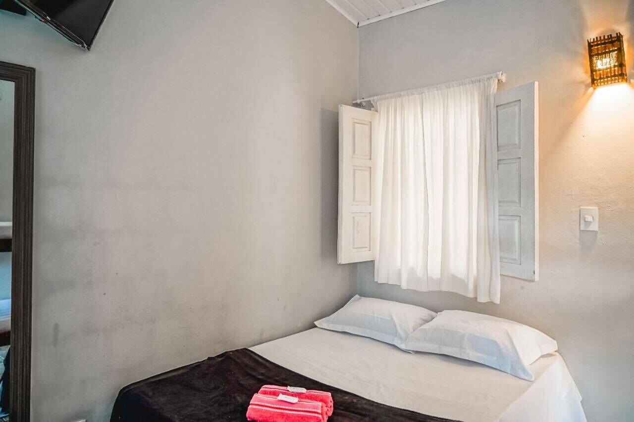 Un dormitorio con cama, cortinas blancas, una lámpara de pared y un espejo.