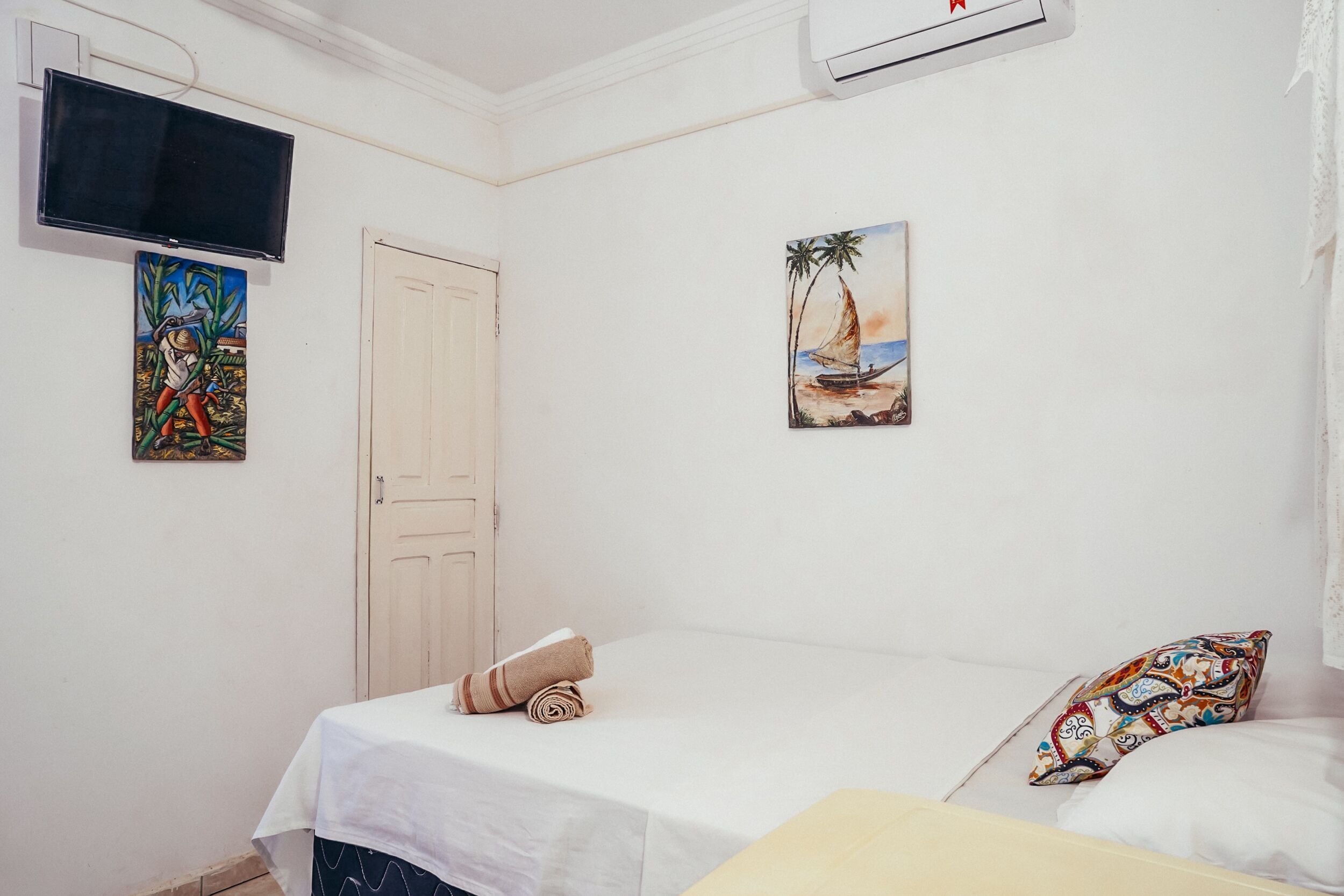 A bedroom with a bed, a TV mounted on the wall, and a painting of a sailboat.