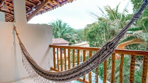 Una hamaca en un balcón con vista a palmeras y una piscina.