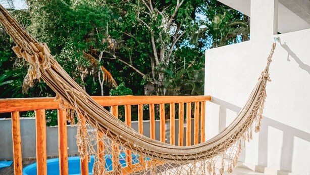 Una hamaca en un balcón de madera con una piscina al fondo.