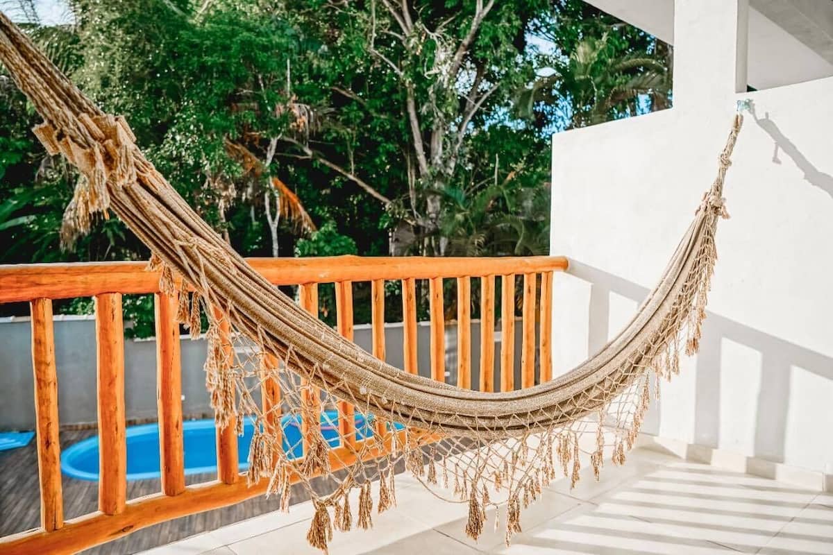 Un hamac sur un balcon en bois, avec une piscine en arrière-plan.