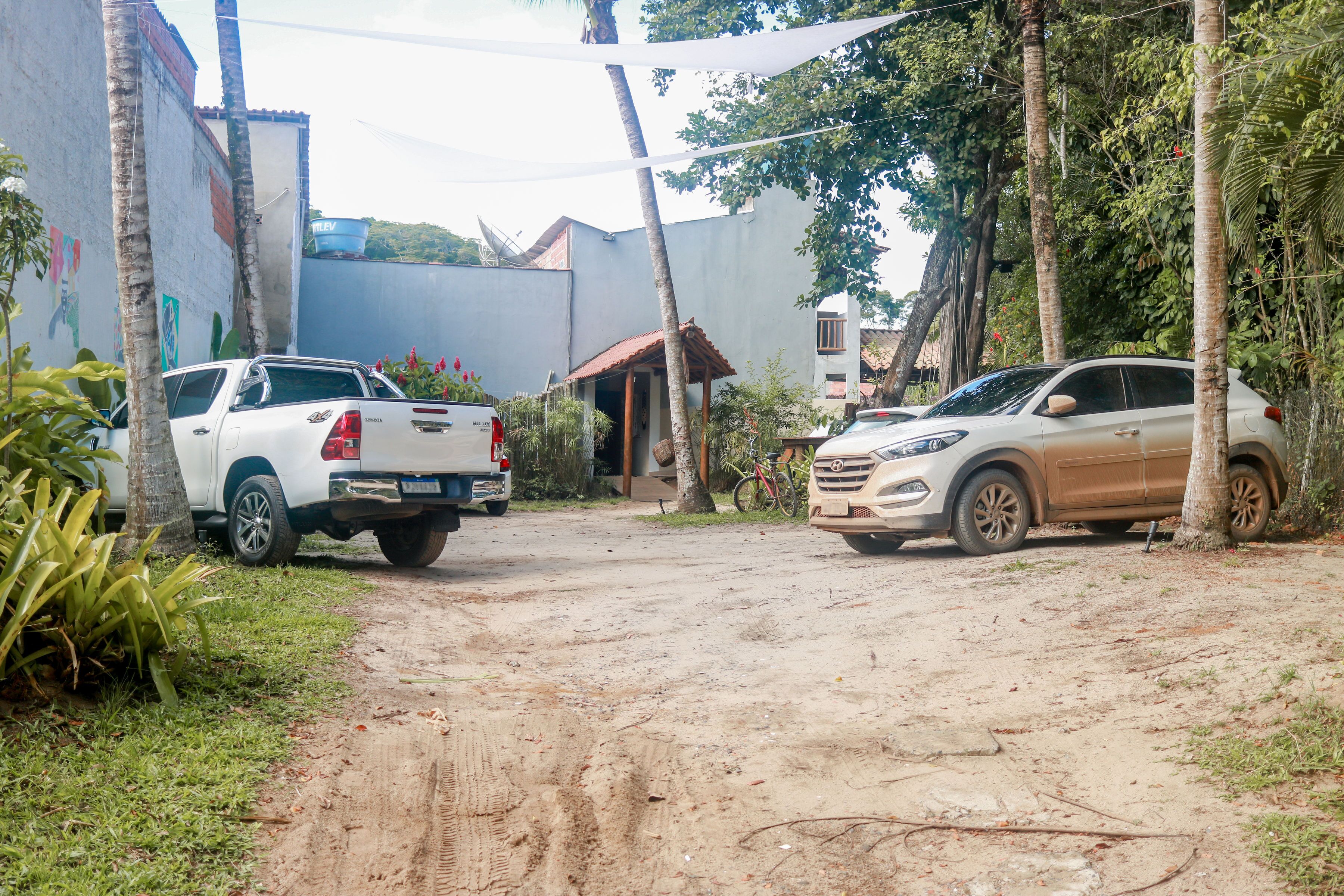 A dirt road leading to a gated entrance with a building and parked vehicles.
